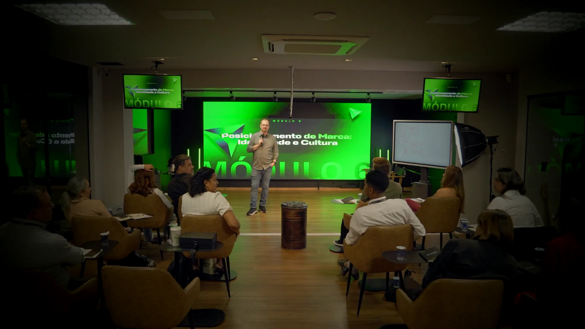 Palestrante no palco do OP!S Hub com painel de LED e TVs de apoio
